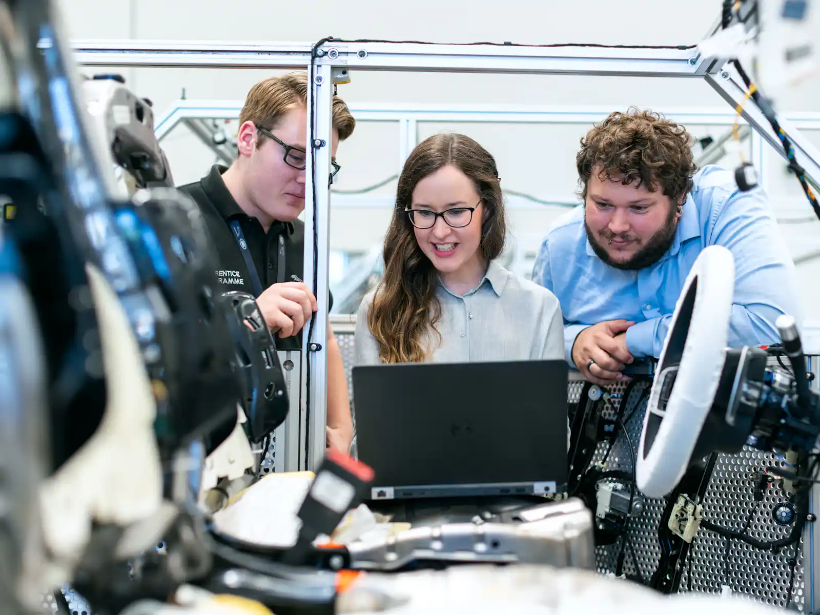 Three colleagues reviewing work together on a laptop beside industrial equipment